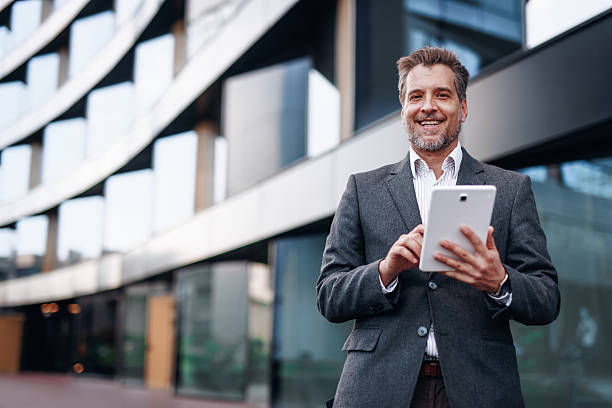 istock Smiling businessman using digital tablet in front of modern office building 2212123635
