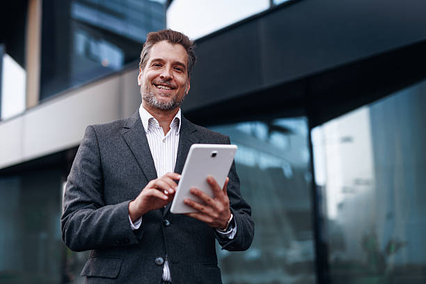istock Smiling businessman using digital tablet in front of modern office building 2212123668