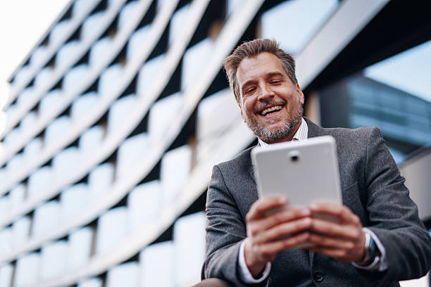 istock Businessman smiling and using digital tablet in front of modern building 2212123700
