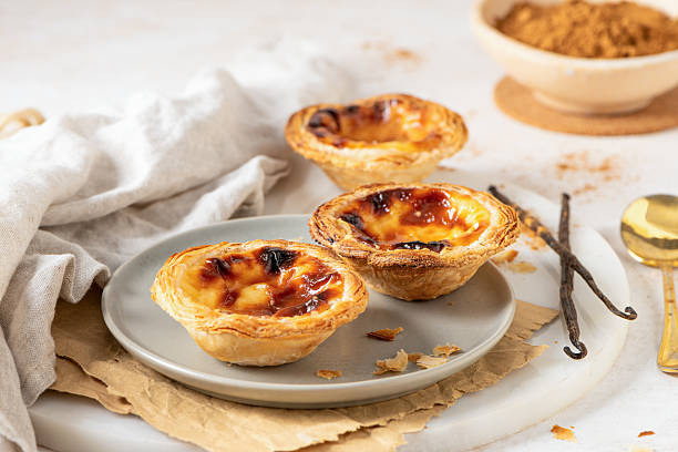 istock Three Pastel de Nata, Portuguese custard tarts, are presented on a plate with cinnamon and vanilla beans. 2212125577