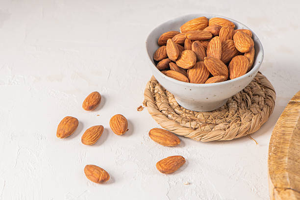 istock Bowl of almonds on a woven mat, with some almonds scattered on a white surface, showcasing a healthy snack option in a rustic setting 2212126218