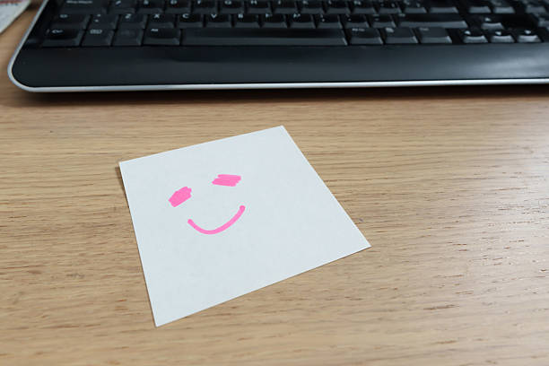 Cheerful pink smiley drawing decorating bright yellow sticky note against wooden desk surface
