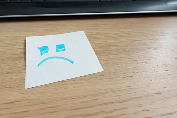 istock White note with a sad face that expresses disappointment, placed on an office desk. Sticky notes 2212127373