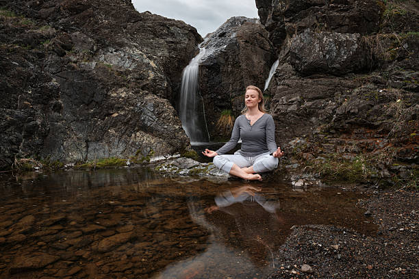 istock Woman meditating by the waterfall in the forest 2212128456