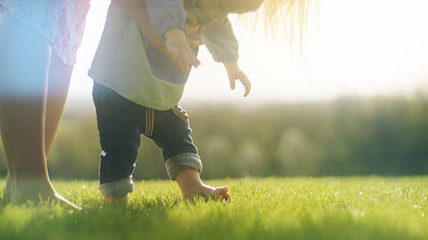 istock Baby Boy Taking First Steps on Sunlit Grass With Parent Support 2212129577