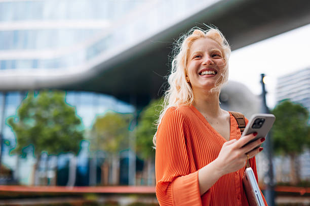 Smiling young student walking in the city using her smartphone