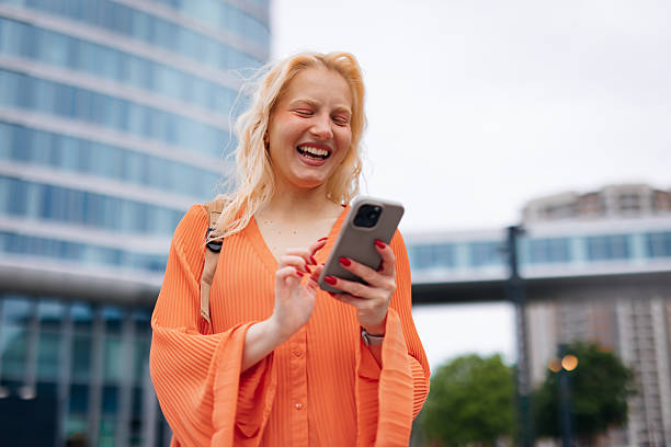 istock Young blonde woman laughing while using mobile phone in the city 2212135418