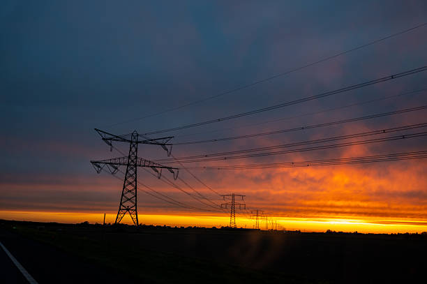 Electricity pylons silhouetted against a vibrant sunset sky