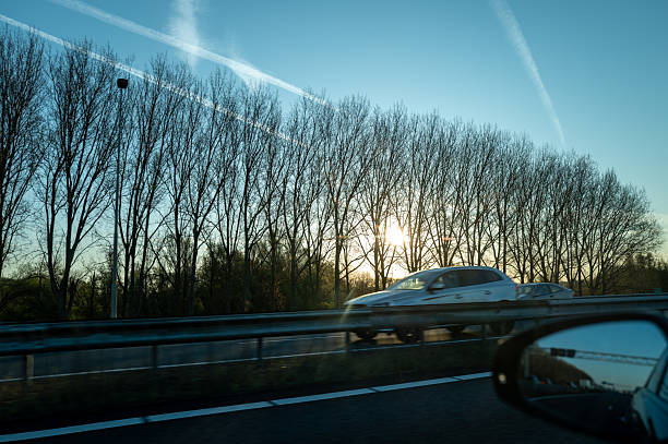 Car driving on the highway at sunset, with trees and contrails in the background