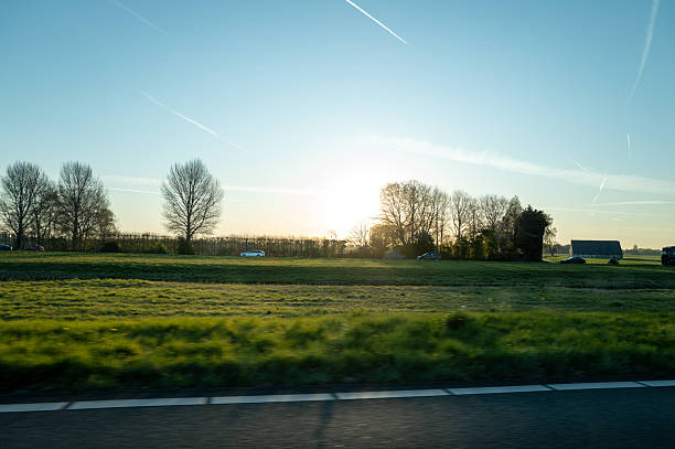 Driving on the highway at sunset near countryside fields and farm