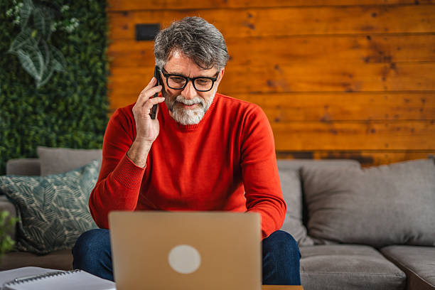 istock Modern senior man sit on sofa with laptop and talk on mobile phone 2212142828