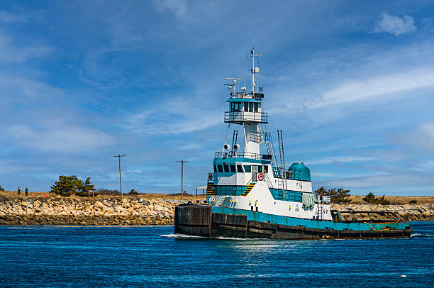 Sandwich, Massachusetts, USA- April 9, 2025-A blue and white tug boat  sails west on  the Cape Cod Canal in early April pulling a barge behind.