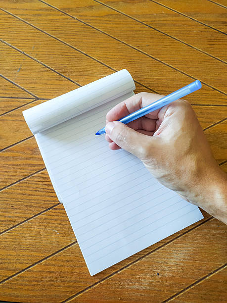 Hand writing on lined notepad with a blue pen on a wooden table. Captures creativity, brainstorming, or notetaking. Use for education, business, or personal growth themes.