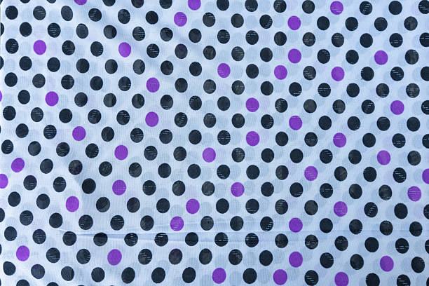 Close-up shot of a light blue fabric with a repeating polka dot pattern The dots are primarily black and purple creating a visually appealing and versatile texture suitable for various design applications The image offers a high-resolution view ideal for seamless pattern use