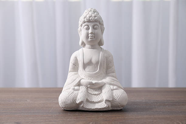 A golden Buddha statue in a peaceful mudra gesture, standing before a colorful temple backdrop, bathed in warm sunlight.