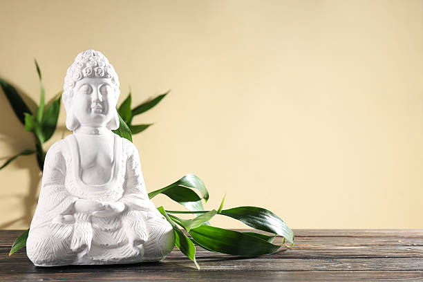 Buddha statue and bamboo on wooden table on beige background, space for text