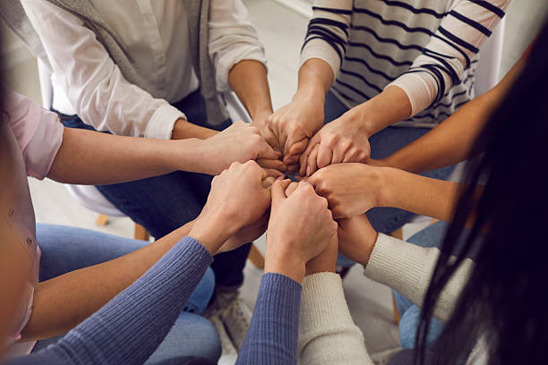 Team of women ready to support each other sitting in a circle and holding their hands stock photo