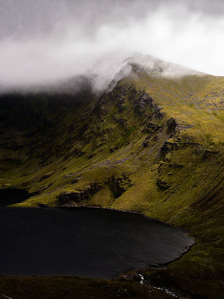 istock Misty mountain peak dramatically overlooks a dark, still lake, creating a serene yet powerful landscape. The contrast between the light and dark is breathtaking. 2212183726
