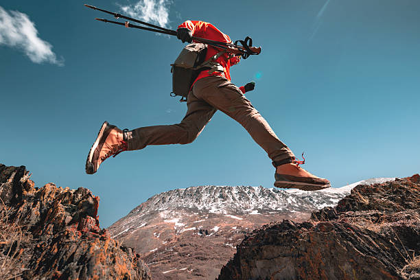 Man hiker with backpack jumps over the hole in mountains