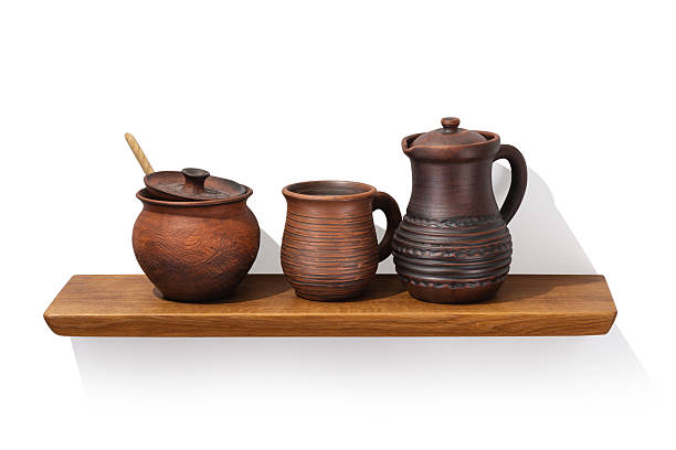 Clay jug with handle, pot and mug on oak wooden shelf isolated on white background, front angle view, design element