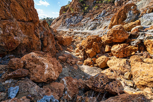 Bright orange, brown, and grey volcanic rocks scattered across rugged cliffs under a sunny sky at Sousaki Volcano near Corinth, Greece.