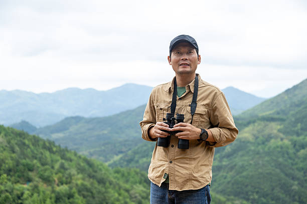 istock Man watching birds using binoculars on top of mountain 2212198886