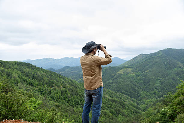 istock Man watching birds using binoculars on top of mountain 2212198906