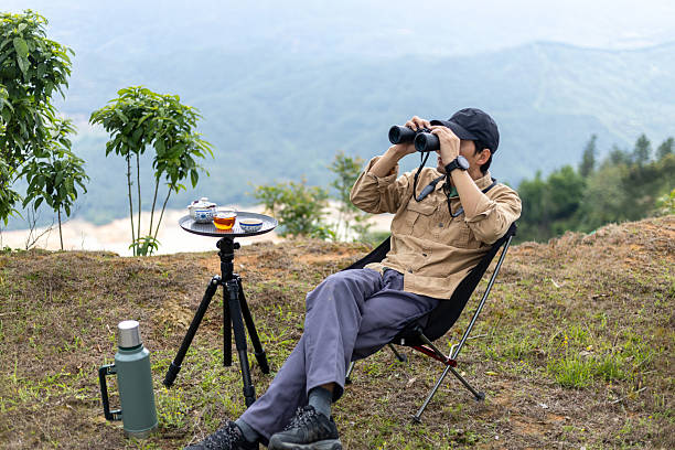 istock Man drinking tea and resting on the top of a mountain, watching birds with binoculars 2212199045
