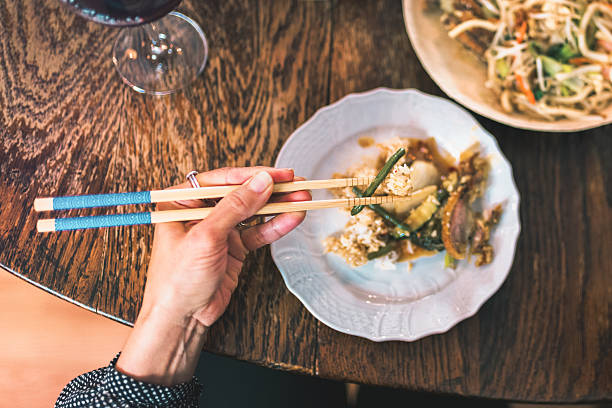 overhead view on female hands holding chopsticks with asian food on lunch table