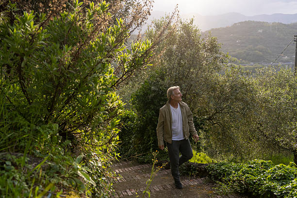Mature man hikes pathway above lush hills at sunrise, springtime, Liguria