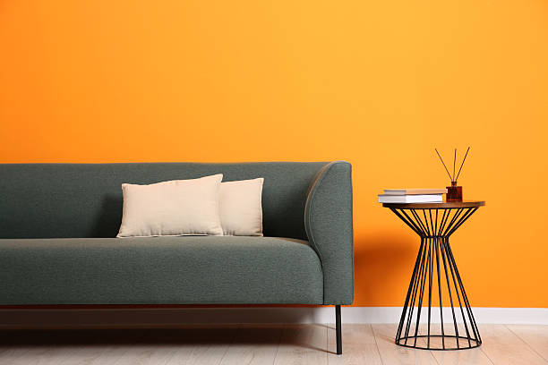 istock Stylish sofa, pillows and side table with decor near orange wall indoors 2212205642