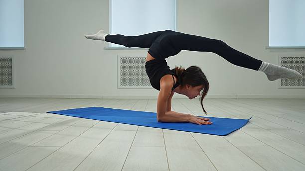 istock Young Woman Performing Advanced Yoga Pose on Blue Mat 2212206571