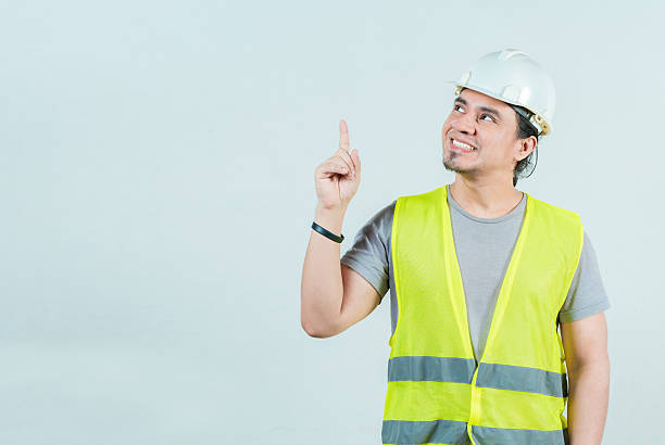 istock Smiling engineer pointing up isolated. Happy young builder with helmet pointing up 2212208636