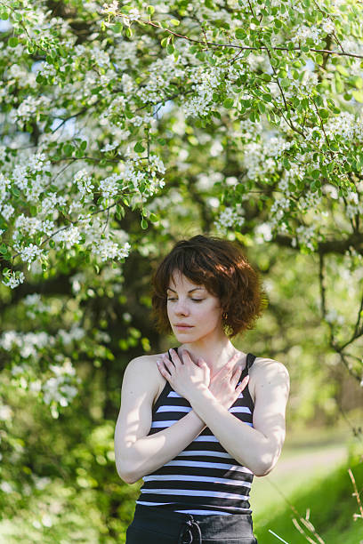 istock Woman standing under blooming tree, touching chest with hands. 2212209992