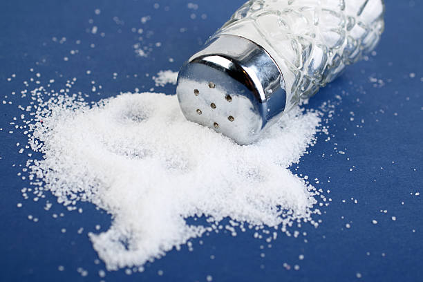 Glass salt shaker lying on top of salt