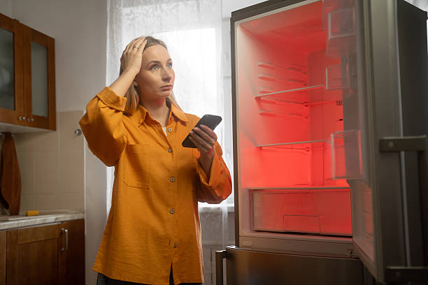 Woman calling refrigerator repair service using smartphone in kitchen stock photo