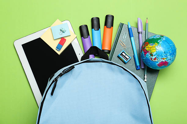 istock Light blue school backpack with stationery on green background, top view 2212214788