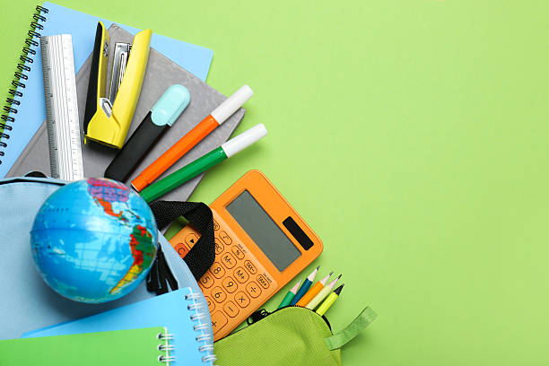 istock Light blue school backpack with stationery on green background, top view. Space for text 2212214789