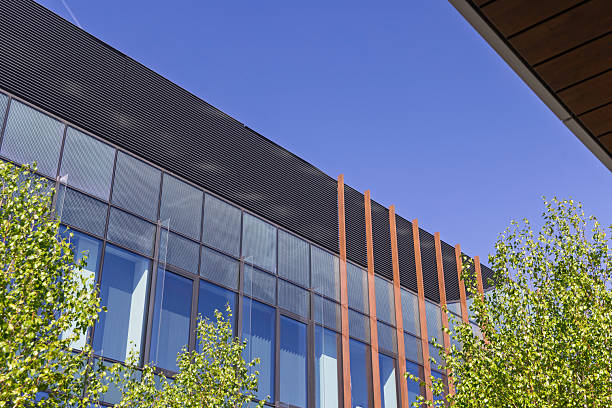 A contemporary building features large glass windows and distinct vertical accents amidst lush greenery, showcasing the intersection of nature and modern architecture.