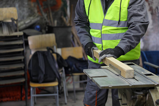 Older man carefully shaping a wooden plank using a woodworking machine. Manual skills, craftsmanship, traditional woodworking, senior carpenter at work.