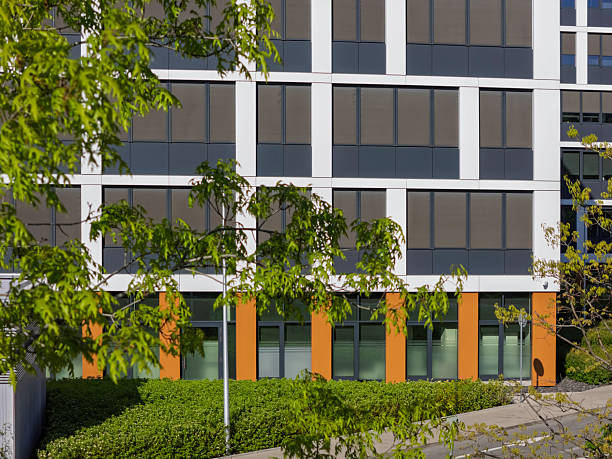 A contemporary building features an arrangement of large windows and smooth lines, complemented by decorative landscaping that enhances the urban environment in broad daylight.