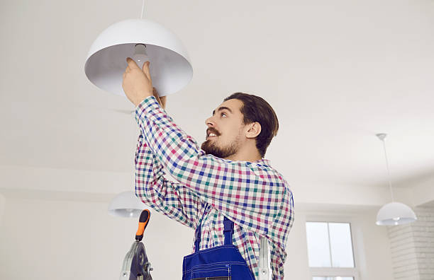 istock Young electrician standing on ladder and changing LED light bulb in ceiling lamp 2212215837