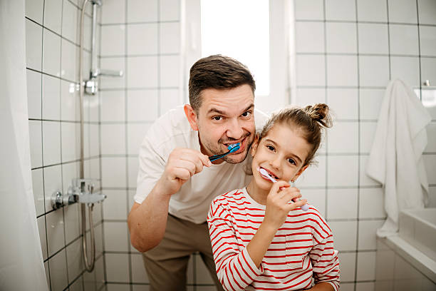 istock Daughter and father brushing teeth together 2212218187