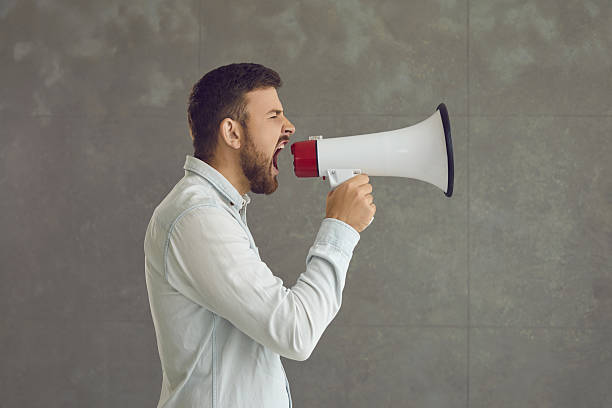 istock Casual adult man shouting in megaphone loudspeaker studio shot with copy space 2212218975