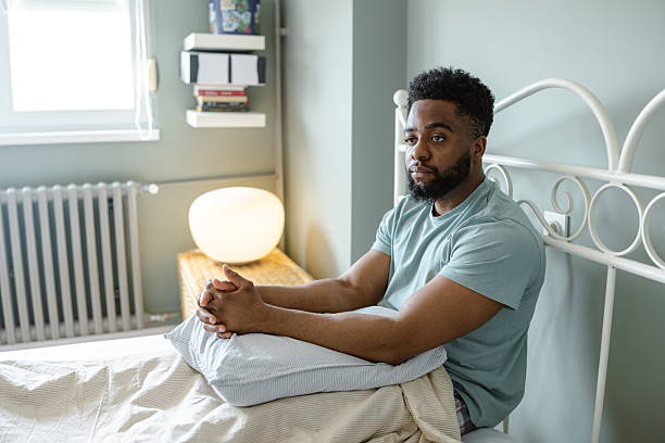 istock Man sitting on a bed thoughtfully in a cozy bedroom 2212225293