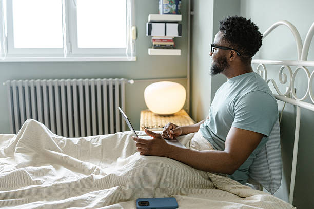 istock Man relaxing in bed while using a laptop in a cozy bedroom 2212226358