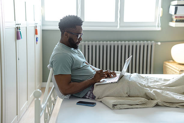 istock Man working on a laptop at home seated on a comfortable bed 2212228568