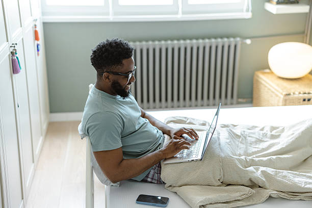 istock Man working on a laptop at home seated on a comfortable bed 2212228644
