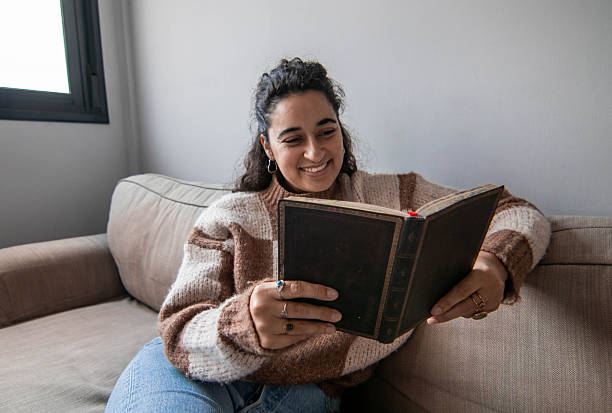istock A woman is sitting on a couch reading a book 2212236838
