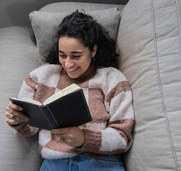 istock Brunette girl sitting on sofa while reading and laughing 2212236896